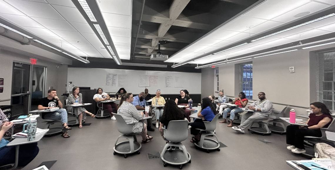 Group of seven people sitting in a circle talking while an outside group of people observe.