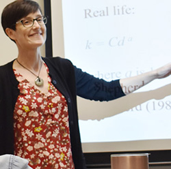 Smiling instructor gestures toward a projected presentation slide.