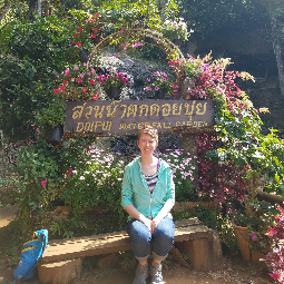 Girl in a sweater sits in nature in front of a sign