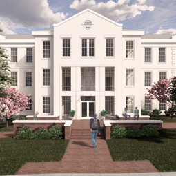 Three story residence hall in off white with student walking on a brick walk way to the front door