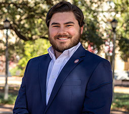 a photo of a man smiling outside with a navy blazer on