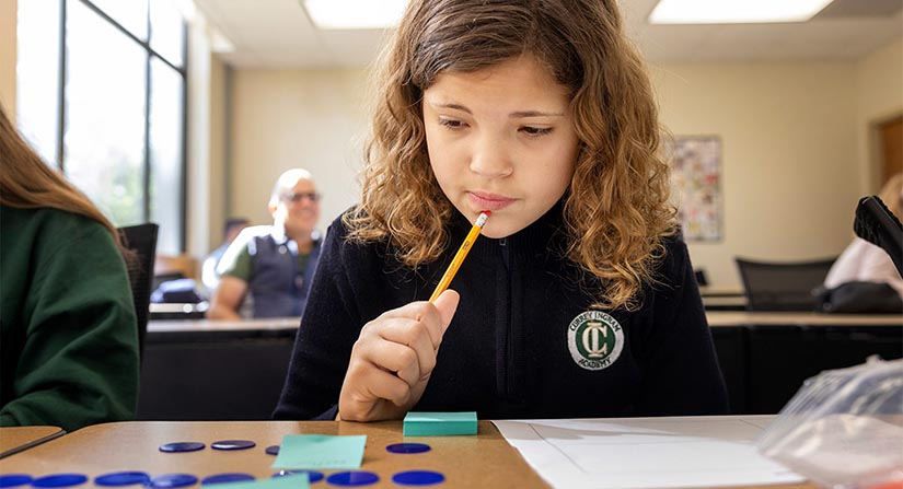 student sitting at a desk pressing a pencil to her chin while she thinks