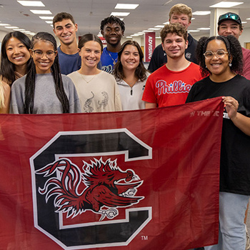 Smiling students pose with a flag featuring the Block C logo