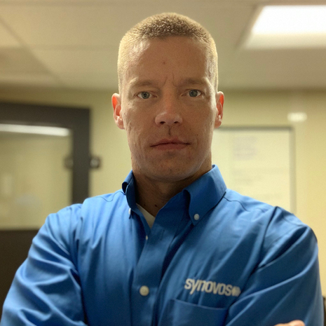 Photo of Derrick Brosius in Synovos shirt in their breakroom