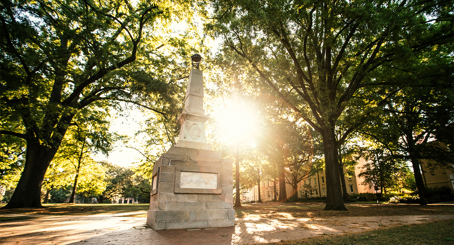 The sun shining through the trees behind the Maxcy Monument on the Historic Horseshoe.