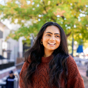 Head and shoulders image of a woman standing outside with building and trees in the background.