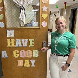 Sophia Comose stands next to a decorated classroom door that reads, 