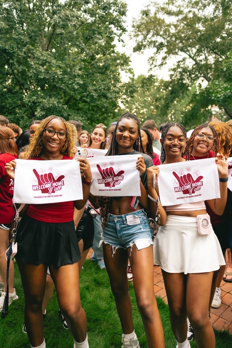 Three girls holding up "Welcome Home" ralley towels
